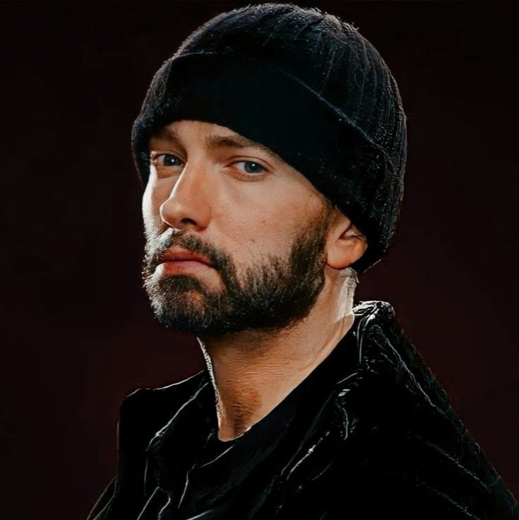 a man with a beard wearing a beanie looking off to the side in front of a red background