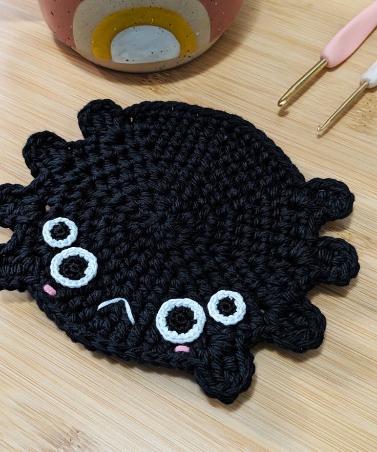 a crocheted black cat rug sitting on top of a wooden table next to scissors