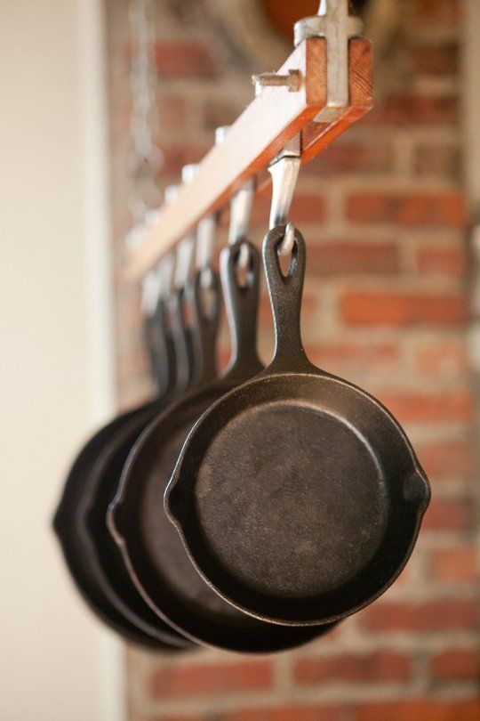 pots and pans hanging from hooks in front of a brick wall