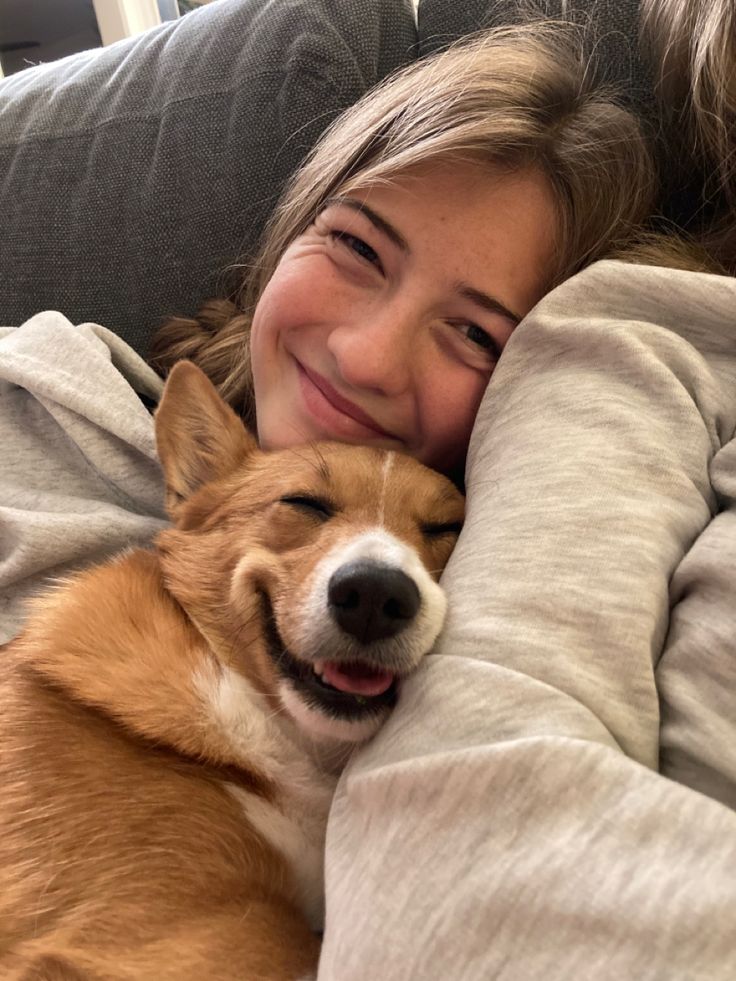 a woman laying on top of a couch next to a brown and white corgi