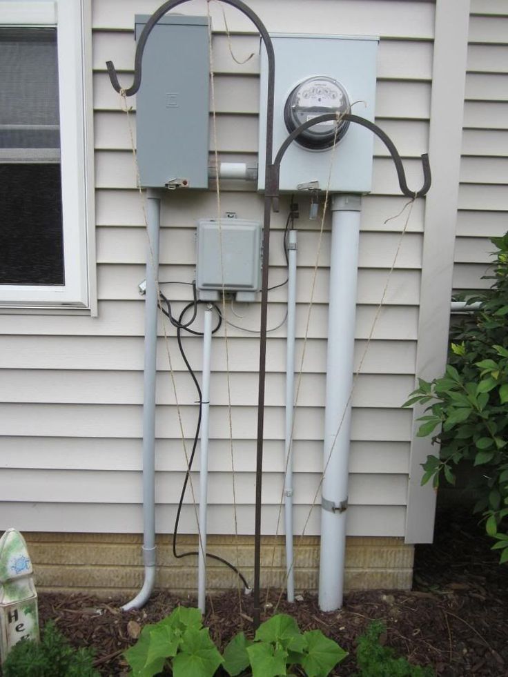 an electric meter is attached to the side of a house with plants growing around it