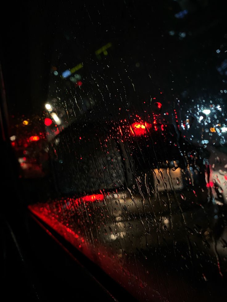 the back window of a car at night with rain on it and street lights in the background