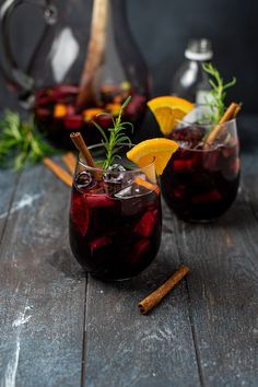 two glasses filled with red wine and garnished with orange slices, cinnamon sticks and herbs