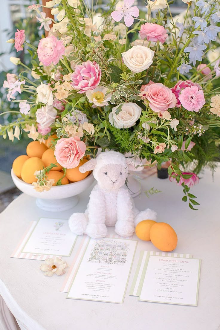 an arrangement of flowers, oranges and a stuffed animal on a table with cards