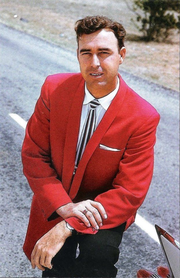 a man in a red suit and tie standing next to a motorcycle on the road