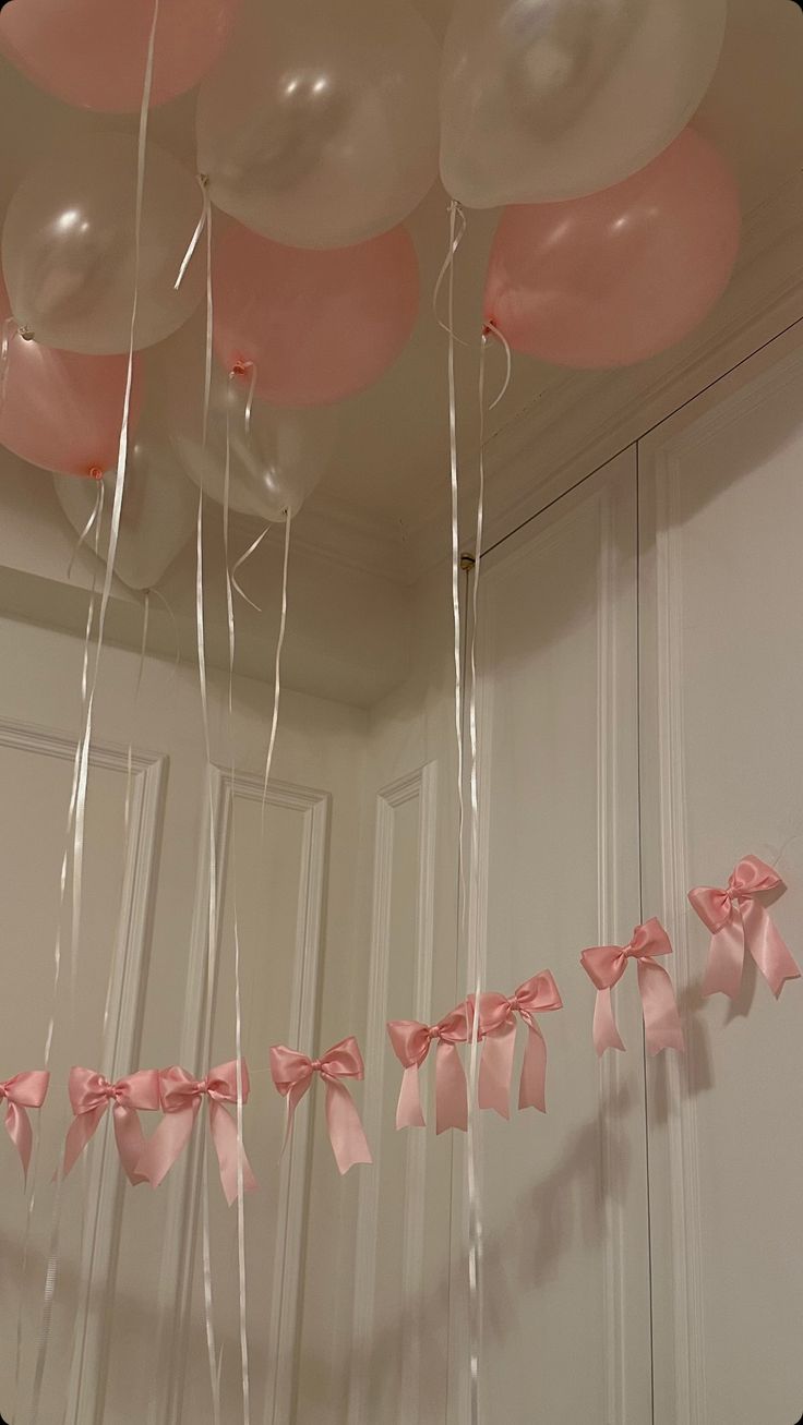 balloons and streamers are hanging from the ceiling in front of a white door with pink bows