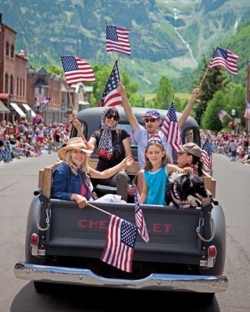 a group of people riding in the back of a pick up truck with american flags