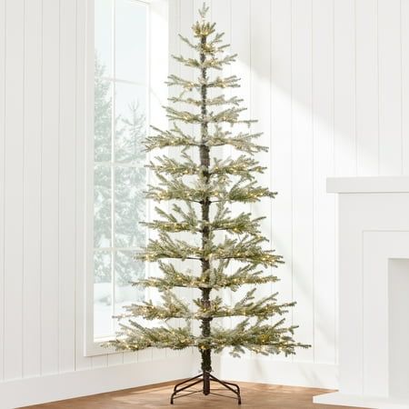 a small christmas tree in a room with white walls and wood flooring, next to a fireplace