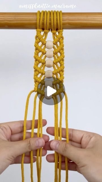 two hands are holding up some yellow string with white beads on it and one hand is knitting