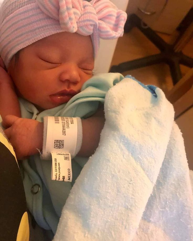 a newborn baby wrapped in a blue blanket and wearing a pink headband with a tag on it's ear