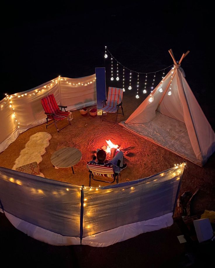 two people sitting in chairs around a campfire with lights on the ground next to them