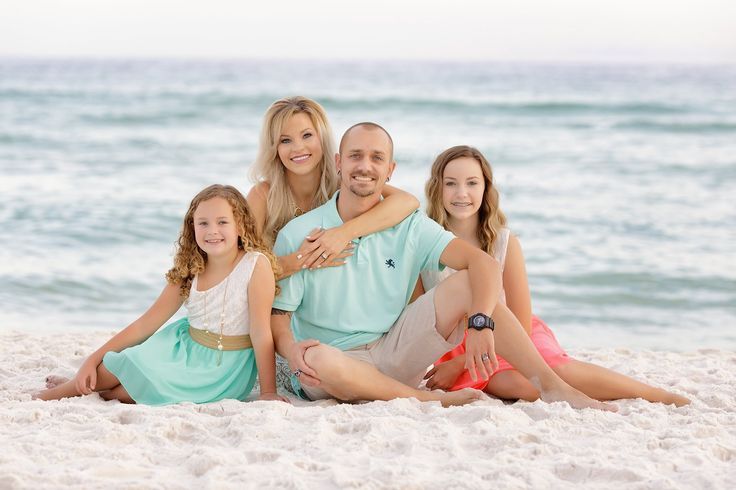 a family sitting on the beach in front of the ocean with their arms around each other