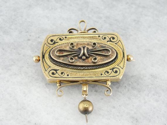 Absolutely stunning workmanship makes this Victorian era brooch all the more beautiful. The classical motif of the top is decorated with black enamel and wonderful texturing, and the textured bead dangle hangs perfectly. Ornate, gothic, and still sophisticated, this unique brooch would be a great piece to wear on just about any occasion! Love this piece but want to make it more versatile, we here at Market Square Jewelers along with our master metalsmiths can convert this fantastic brooch into a Ornate Engraved Brooch, Victorian Brooches With Locket Pendant, Victorian Locket Pendant Brooches, Ornate Locket Brooch For Formal Occasions, Gold Coin Jewelry, Victorian Brooch, Unique Brooch, Market Square, Gold Brooch