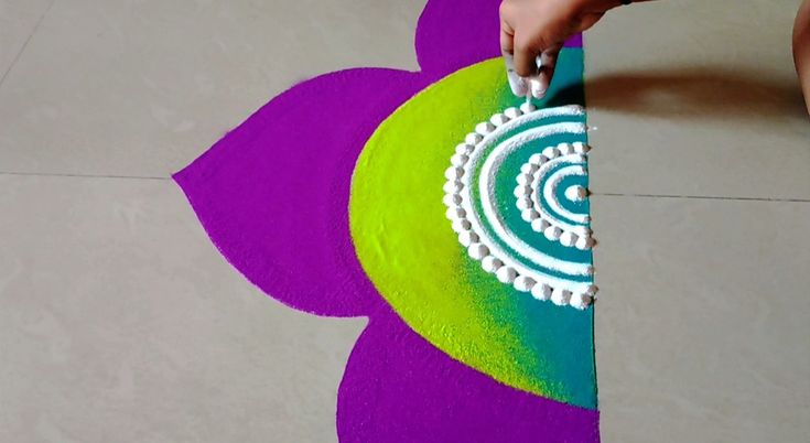 a person cutting paper with scissors on top of a flower shaped tablecloth that has been painted purple, green and yellow