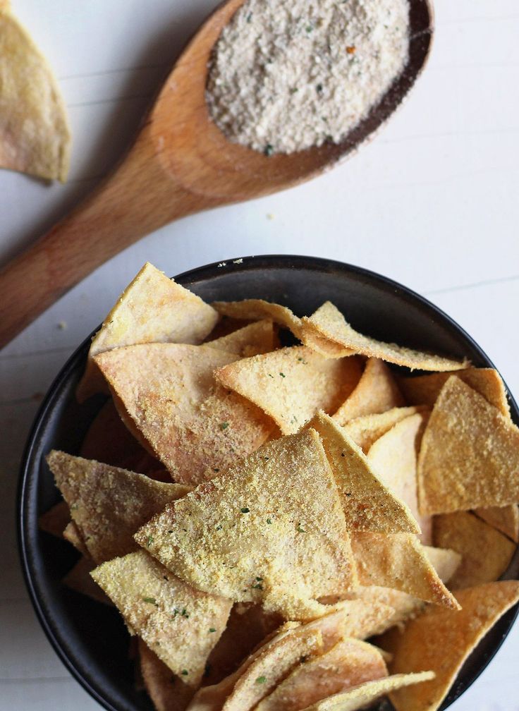 a black bowl filled with chips next to a wooden spoon on top of a table