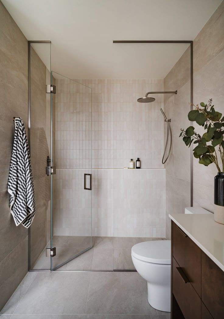 a bathroom with a white toilet sitting next to a walk in shower and a plant