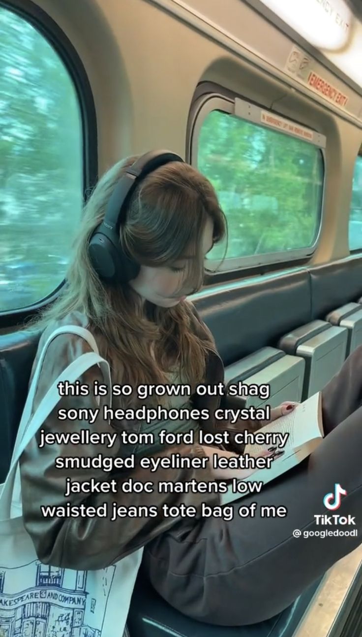 a woman sitting on a train with headphones and looking at a book in her hand