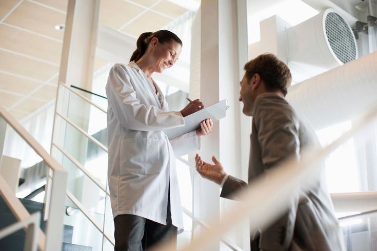 a man and woman in business attire standing on stairs talking to each other while holding papers