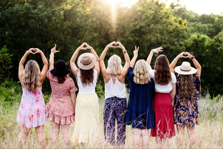 four girls are standing in a field with their hands up and the sun shining behind them