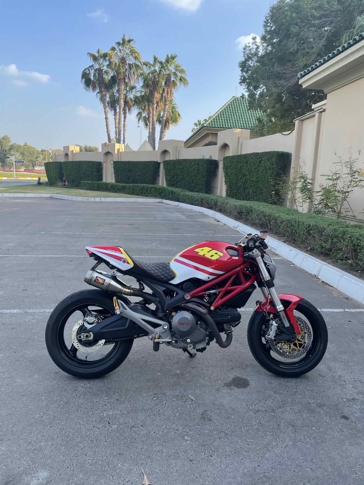 a red and white motorcycle parked in a parking lot next to palm trees on a sunny day