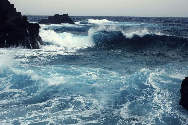 large waves crashing on the rocks in front of an ocean cliff with dark blue water