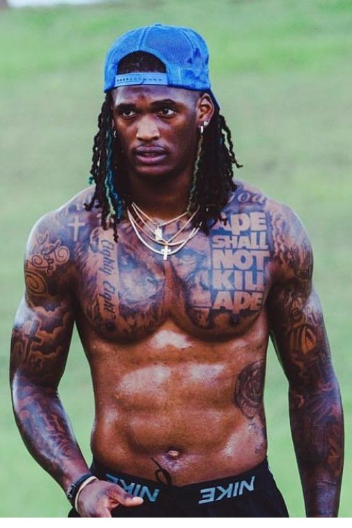 a shirtless man with tattoos on his chest standing in front of a green field