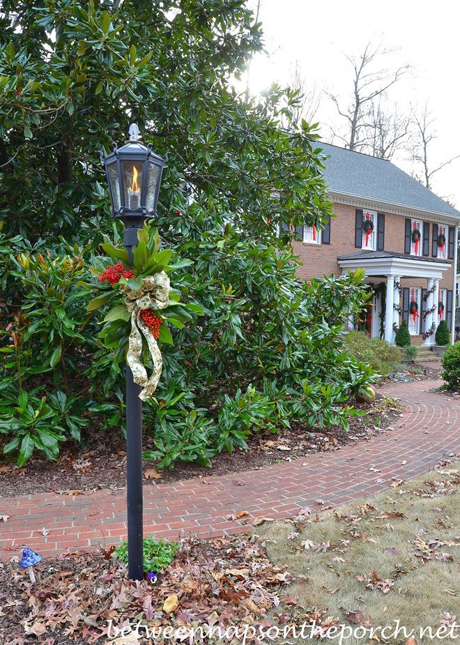 a lamp post with a wreath on it in front of a brick walkway and house