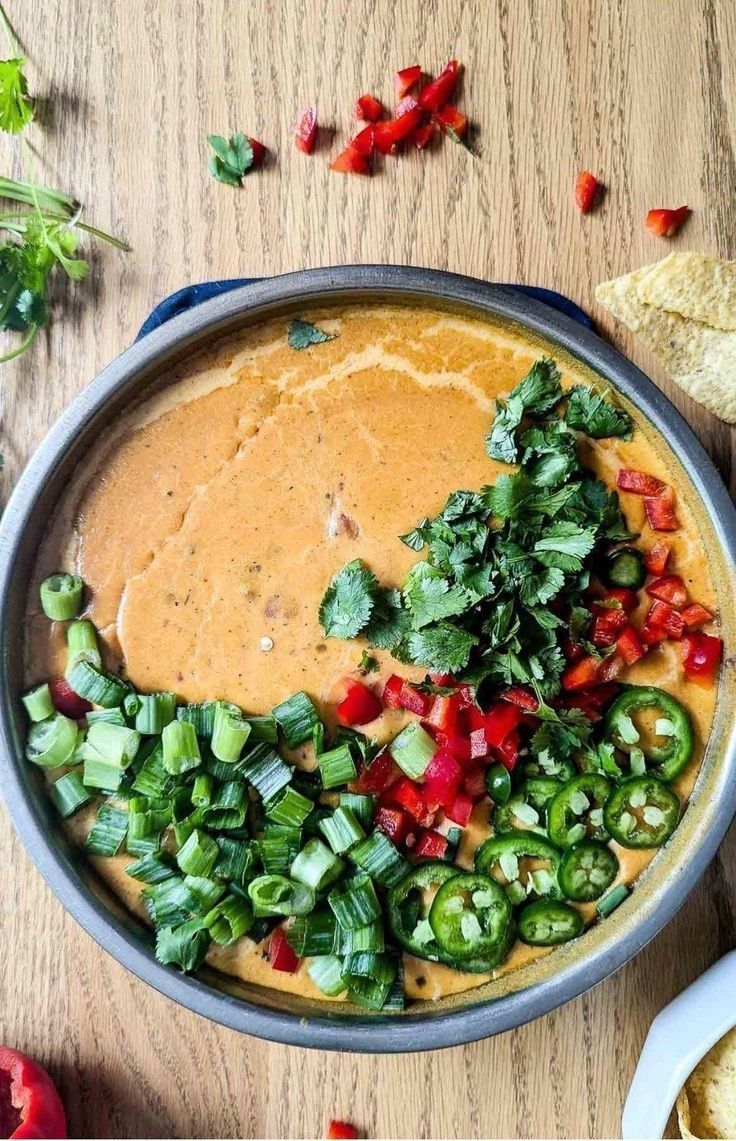 a bowl filled with tortilla chips, salsa and green peppers on top of a wooden table