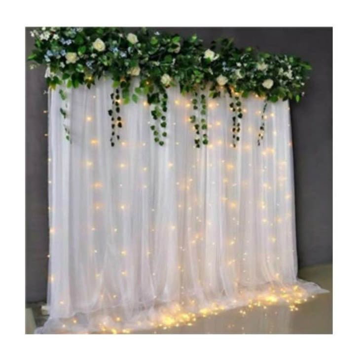 white flowers and greenery are hanging over the sheer curtain with fairy lights on it