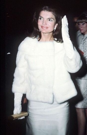 a woman in a white dress and fur coat waves to the crowd at an event