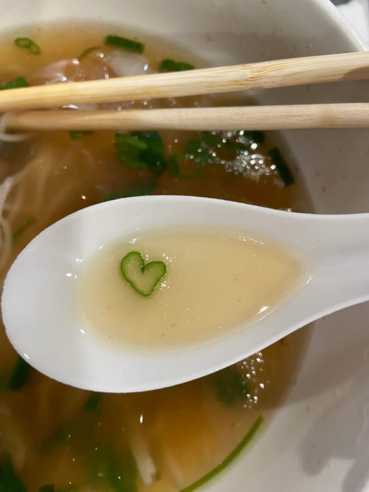 a white bowl filled with soup and two chopsticks on top of the bowl