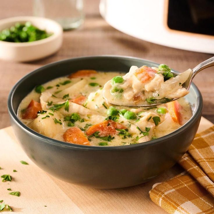 a bowl of chicken and dumpling soup with a spoon in it on a wooden table