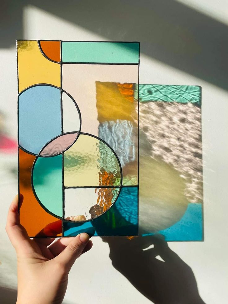 a person holding up a piece of art made out of stained glass with circles on it