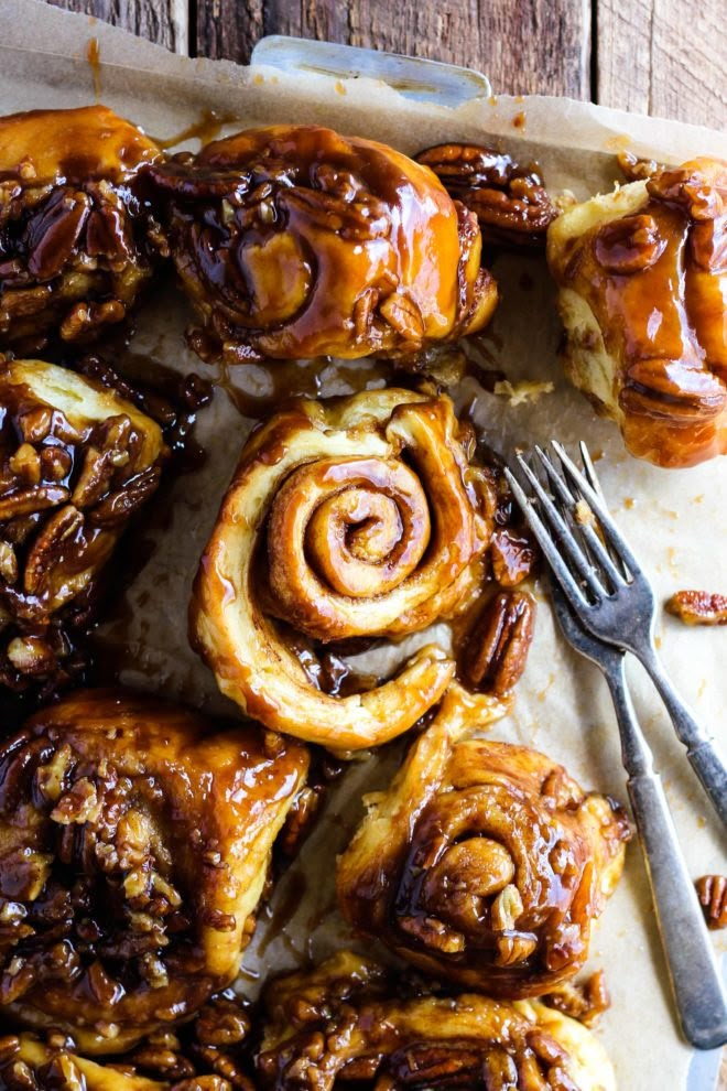 cinnamon buns on parchment paper with fork and knife next to them, ready to be eaten