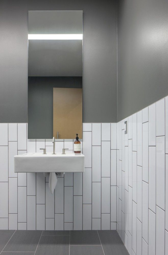 a bathroom with gray and white tiles on the walls, sink and mirror in it