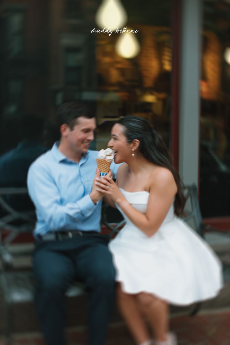 a man and woman sitting on a bench eating an ice cream cone in front of a building