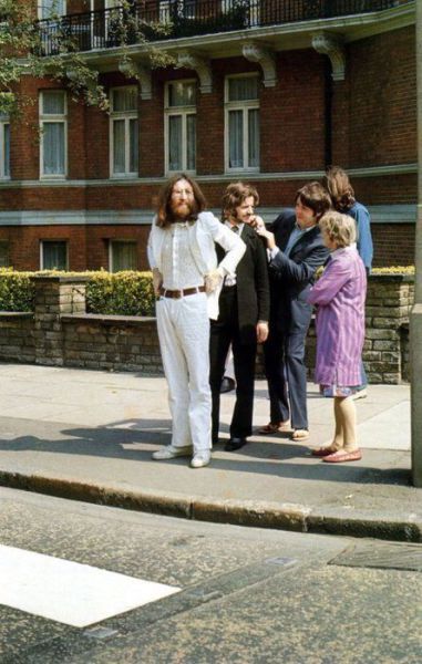 some people are standing on the side walk talking to each other and one person is wearing a white suit