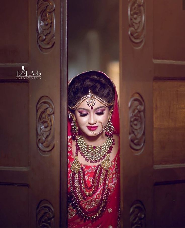 a woman in a red bridal outfit looking out from behind a wooden door with ornate carvings on it