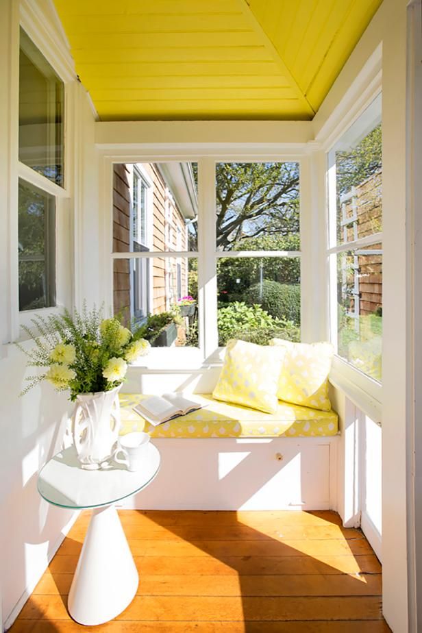 the sun shines brightly through the windows in this sunny porch with white furniture and yellow cushions