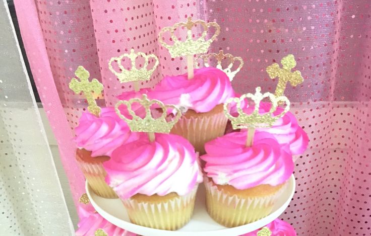 there are cupcakes with pink frosting and gold crowns on the cake stand