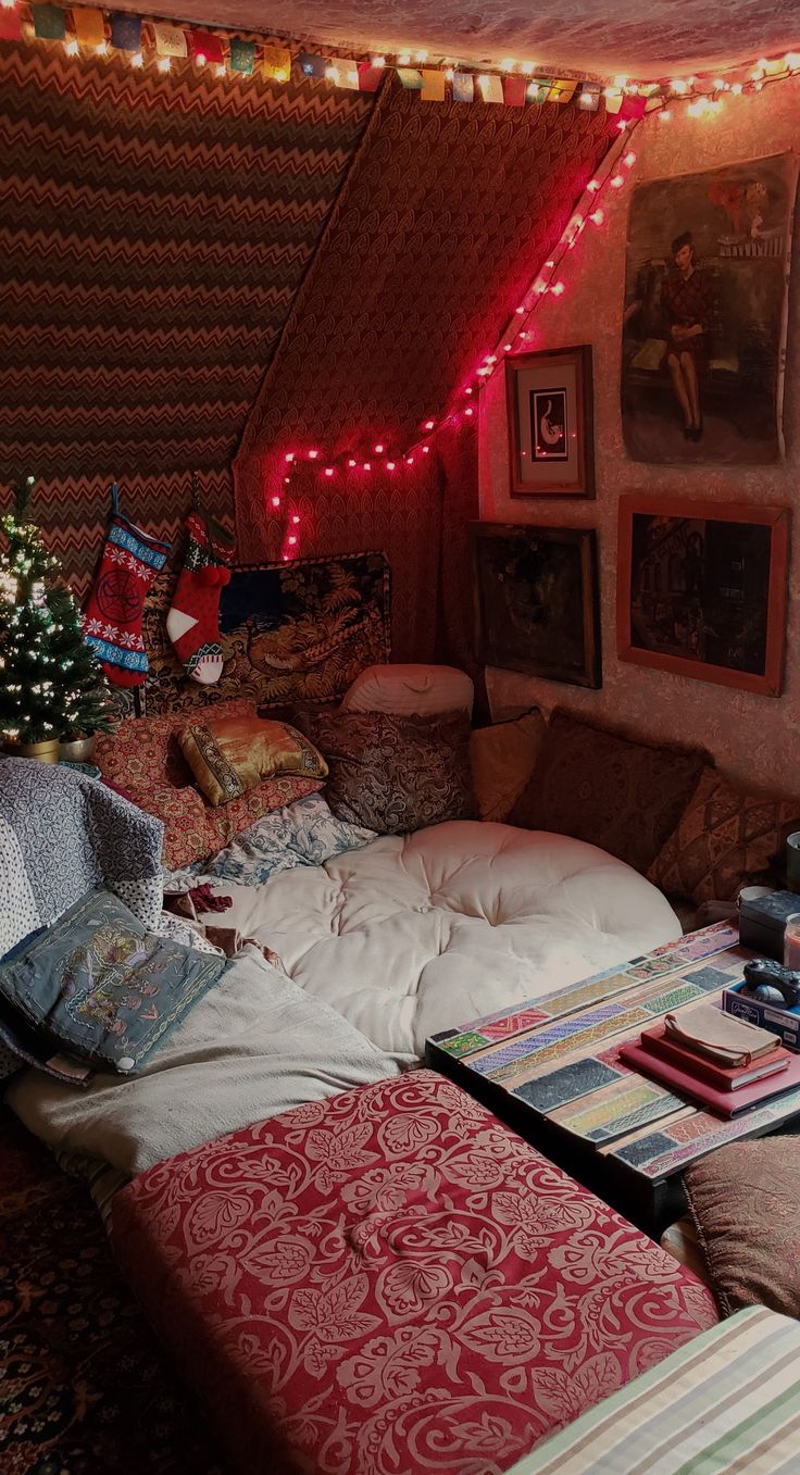 a bed room with lots of pillows and blankets on the floor next to a christmas tree