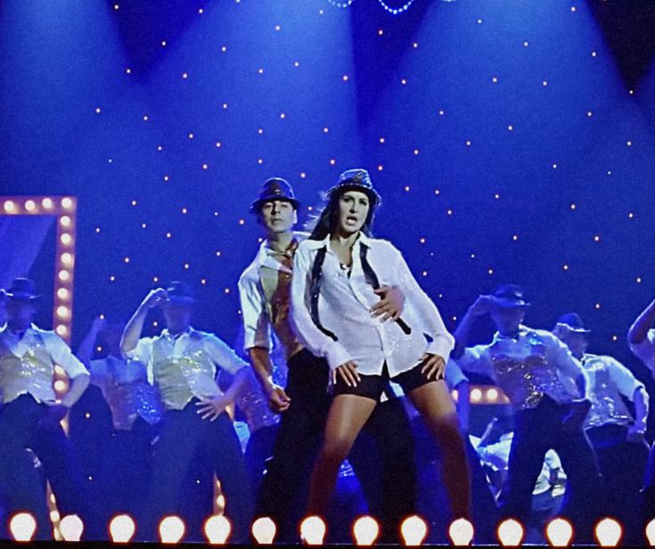 two men in white shirts and black ties on stage with lights behind them as they dance