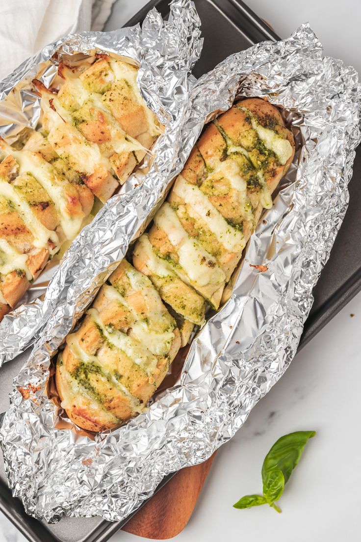 two pieces of bread covered in cheese and pesto on top of aluminum foil, sitting on a cutting board