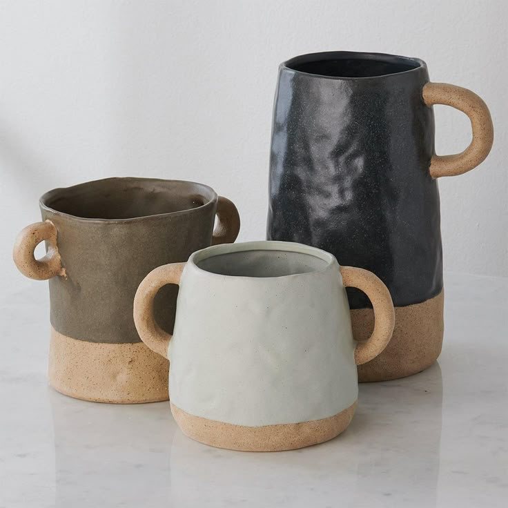 three different colored mugs sitting next to each other on a white counter top,