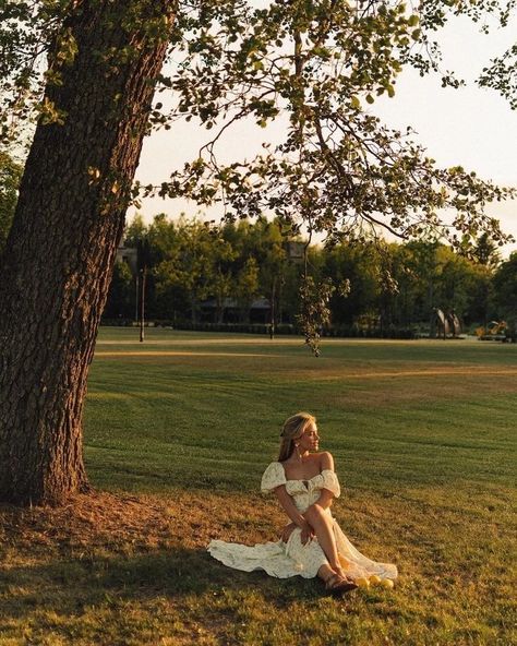 a woman sitting under a tree in a field