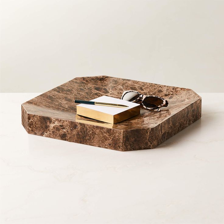 a marble tray with a pair of sunglasses and a book on it, sitting on a white surface