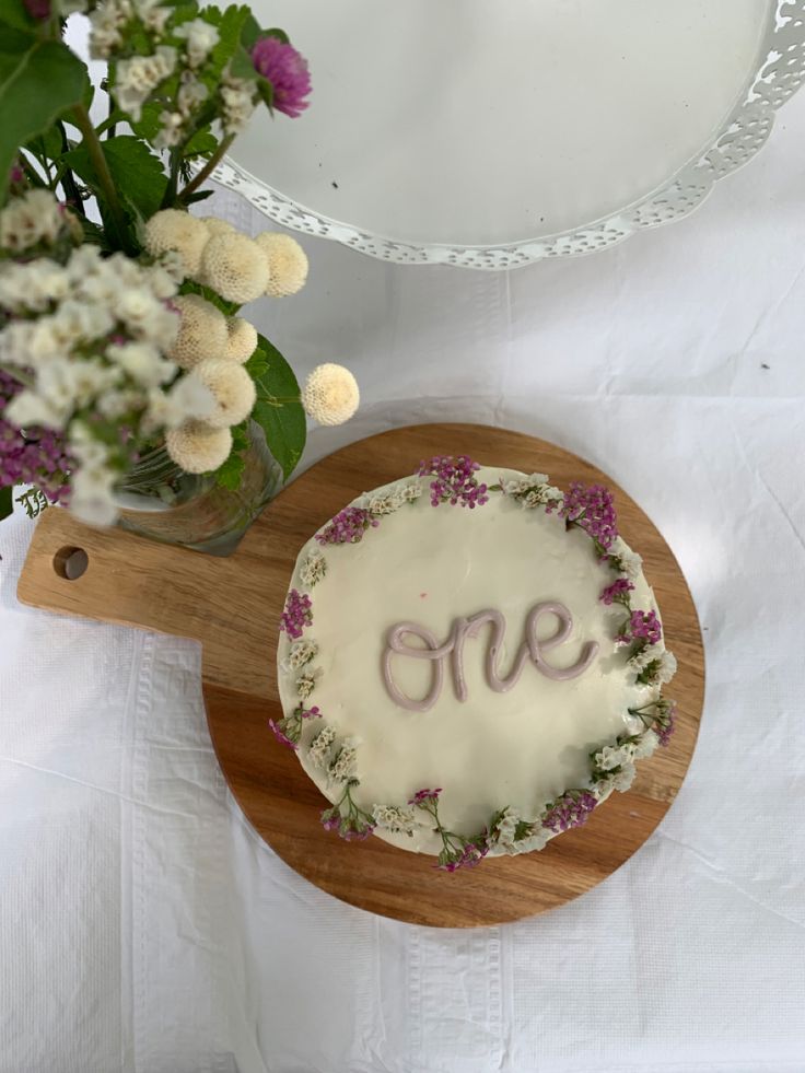 a cake with the word one written on it sitting next to a plate and flowers