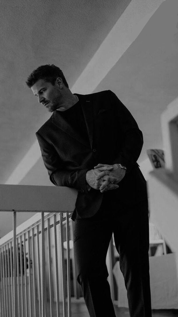 a man in a suit leaning on a railing looking down at his hand while standing next to him