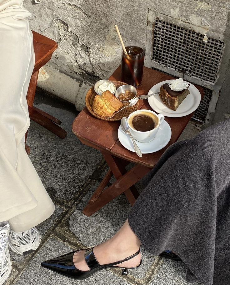 two people sitting at a table with coffee and pastries on it, one woman is wearing high heels