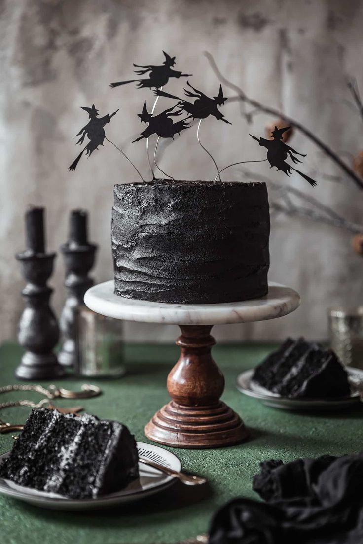 a black cake sitting on top of a table next to other desserts and candles